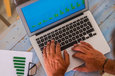 Ofisteki bilgisayarla istatistik ve grafiklerle dolu mavi ahşap bir masa üzerinde yazma ve çalışma ellerini kapat. 