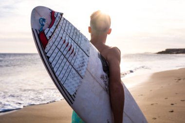 Sahilde sörf tahtasıyla koşan adamı yazın gün batımında sörf yapmaya giderken yaklaş. 
