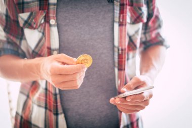 Genç kız ayakta durup Bitcoin ile oynuyor ve telefonuna bakıyor. 