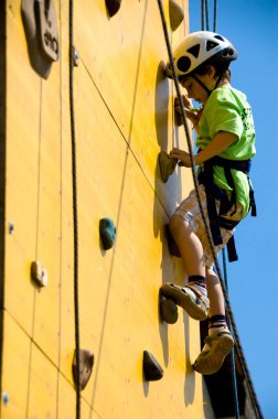 Genç dağcı çocuk duvara tırmanıyor - çocuk tırmanırken tek başına eğleniyor - anın tadını çıkarıyor - arka planda mavi gökyüzü