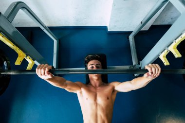 Bedenini spor salonunda çalıştıran, ağırlık kaldırma hareketleri yapan bir genç.  