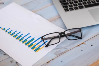 Gözlüğü, bilgisayarı ve grafiği mavi ahşap masa istatistikleriyle kapat - iş adamı ya da kadın yaşam tarzı  