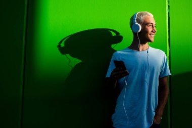 Neşeli ve mutlu bir milenyum. Kulaklıklarıyla müzik dinleyerek eğleniyor ve eğleniyor. Genç adam müzik duyuyor ve yeşil arka planda gülümsüyor. 