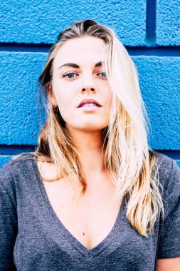 Güzel bir kız mavi arka planlı kameraya bakıyor. Mavi gözlü sarışın bir genç.  