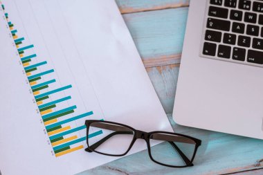 close up of laptop or computer pc with glasses and graphs and statistics on a blue wood table - nobody at the photo  clipart