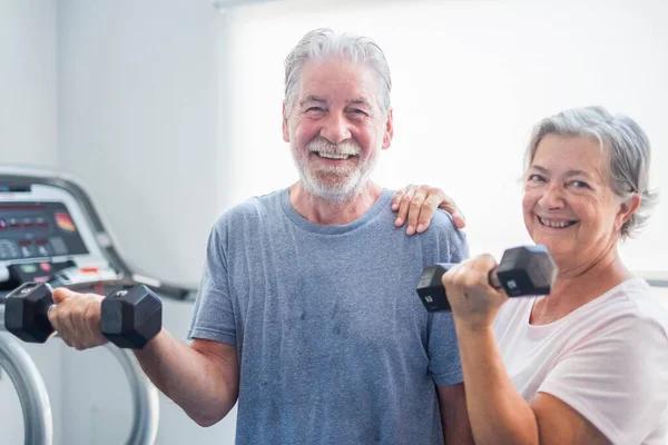 couple of two seniors at the gym holding a dumbbells and with the tapirulan at the background - active mature people together doing exercises