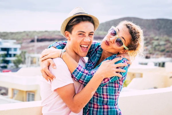 beautiful couple of mum and son together hugged in the terrace of the home having fun and laughing - woman with sunglasses and teenager with a relationship - guy with a hat happy and funny