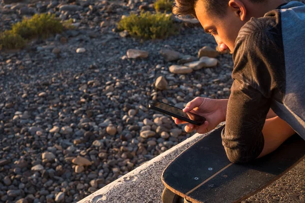 stock image beautiful guy and teenager at the beach alone with his phone - playing, chatting or viewing videos with his skateboard 