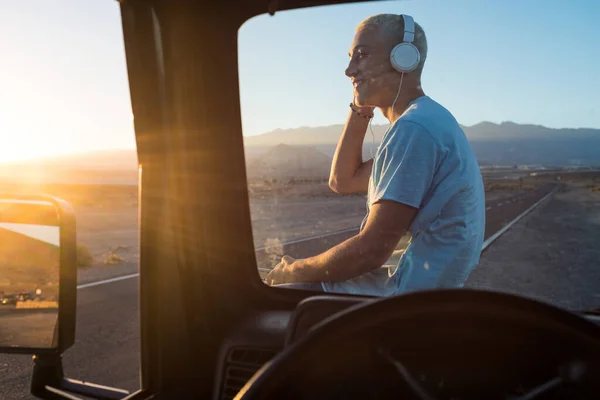 one man alone listening music with his headphones on his car looking at the beautiful landscape sunset - happy cheerful teenager travelling and using his phone on his holiday