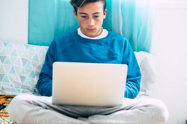 teenager alone at the bedroom on the bed looking videos, working or play video games with his laptop or computer and his phone - online lifestyle and future generations