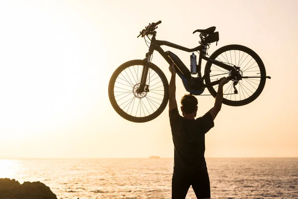 stock image beautiful silhouette of man holding his bike up like a winner at the beach - adult successful concept and lifestyle 