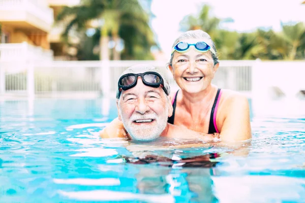 stock image two seniors or mature people together hugged in the blue water of the swimming pool - active woman and man doing exercise together - summertime and having fun 
