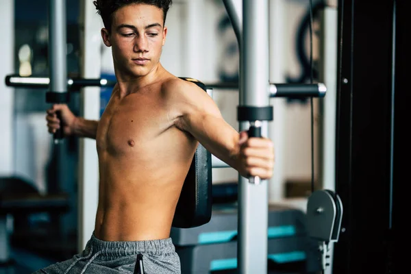 teenager alone at the gym doing exercises and looking his muscles - fitness and healthy lifestyle - athlete training his body to be happy