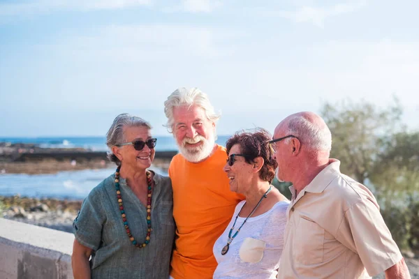 stock image group of four happy seniors and mature people talking and having fun together at the beach with the sea at the background - friendship and relationship concept 