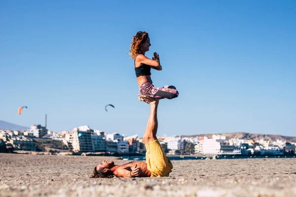 couple of two adults at the beach dong exercise like yoga called acroyoga - man lying on the sand holding a woman with his feet and leg in the air
