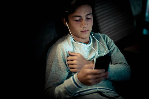 stock image teenager wearing headphones alone at home on the sofa with his laptop working or playing or watching videos