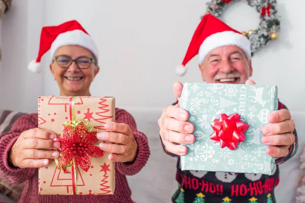 two mature people or seniors at home sitting on the sofa the Christmas day opening and wrapping their presents or gifts together - cheerful and smiling people having fun