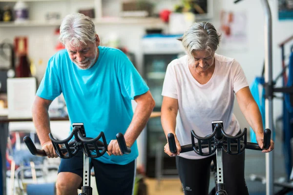 couple of two seniors and mature people on the circlet training at the gym cycling together - active pensioner lifestyle concept - man and woman without stop