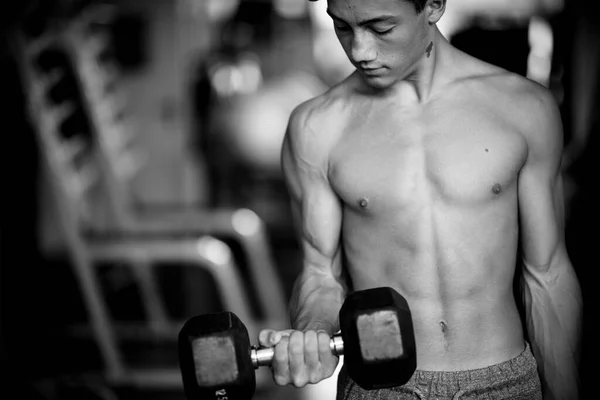 one teenager alone at the gym training and lifting a dumbbells - strong and with muscles man - fitness and muscle lifestyle - picture in black and white