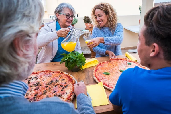 group of people or family at wooden table eating pizza together with two big pizzas - two senior, one woman and one teenager prepared to eat