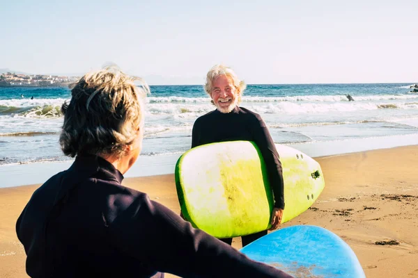 黒のウェットスーツを着た数人の高齢者がビーチをサーフィンする準備ができている アクティブな成熟した引退した人々は休暇や自由な時間で一緒に幸せな活動をしています — ストック写真