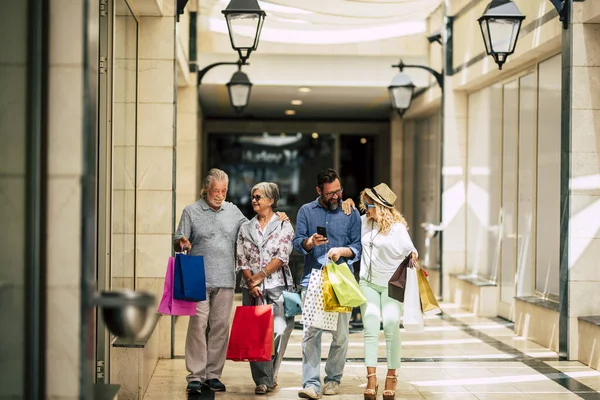 group of people go shopping together with a lot of bags on their arms and holding with hands at mall or big store - family enjoying buying clothes together of doing gifts for Christmas
