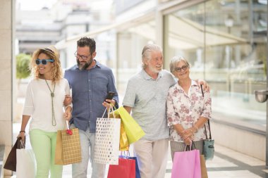 two couples of two adults and two seniors go shopping together at the mall with a lot of bags with clothes and more on their hands - four people happy enjoying     clipart