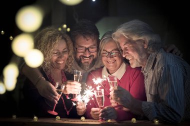 Bir grup son sınıf öğrencisi ve iki yetişkin birlikte havai fişeklerle eğleniyorlar. Yeni yılı kutlamak için. Gece yarısı ışıklarıyla mutlu bir aile. 