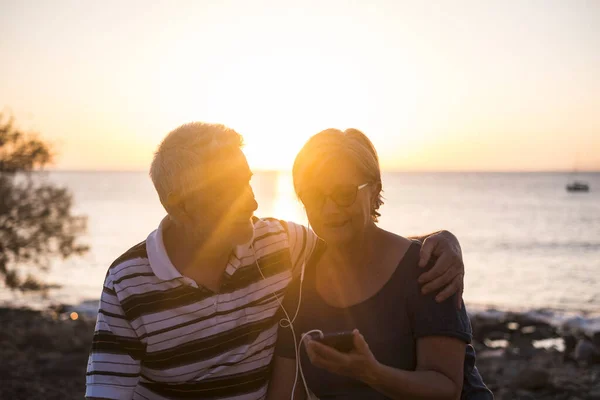 Senior Paar Knuffelen Het Strand Met Zonsondergang Gepensioneerd Stel Luisteren — Stockfoto