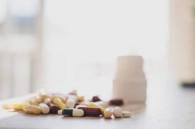 Çok renkli tabletler, haplar, evdeki masanda şişe bulunan kapsüller, masada yığınla ilaç. Farklı renkte ilaçlar ve beyaz laboratuvar masasında haplar.