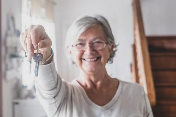 Portrait of happy senior woman holding keys of new home or property. Old lady showing or giving keys to house. Elderly female happy for moving into new apartment