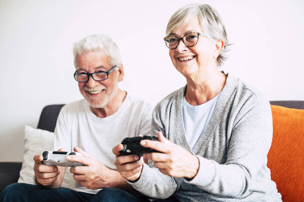 couple of seniors and mature people looking and the tv and using controllers playing video games at home together on the sofa - lockdown lifestyle indoors 