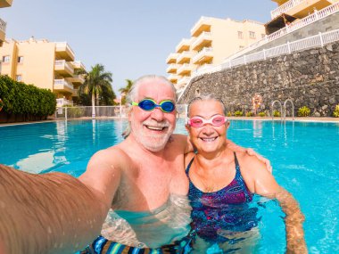 İki mutlu son sınıf öğrencisi yüzme havuzunda birlikte eğleniyor ve fotoğraf çektirip gülümsüyor ve kameraya bakıyor. Mutlu insanlar yazın dışarıda suyun tadını çıkarıyorlar. 