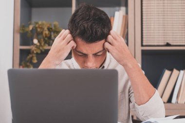 Aşırı çalışma ve sınavlar için çok çalışma yüzünden evde baş ağrısı çeken sağlıksız bir genç adam. Okul için ödev yapmaktan yorulmuş genç bir erkek. 