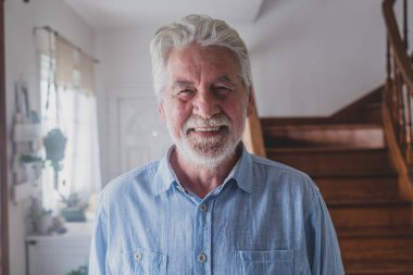 Gri saçlı mutlu yaşlı adam, 80 'li yaşlarda evde beyaz dişleriyle gülümsüyor. İçerde rahatlayan neşeli bir büyükbabanın portresi.. 