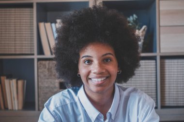 Kıvırcık saçlı, esmer, çekici bir kadının yakın plan portresi. Ofiste gülümseyen Afrikalı Amerikalı iş kadını. Genç pozitif bayan gülümsüyor ve kameraya bakıyor. 