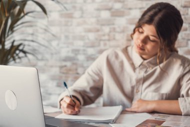 Gülümseyen kadın notlar yazıyor. Dizüstü bilgisayarda webinar çalışmalarını izliyorlar. Genç öğrenci bilgisayar dersi öğreniyor. 
