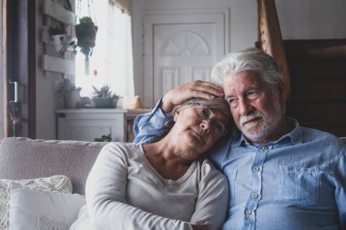 Düşünceli üzgün yaşlı adam ve kadın modern evin oturma odasında kanepede dinleniyorlar. Emekli çift, evdeki kanepede otururken birbirlerini depresyondan rahatlatıyorlar. 