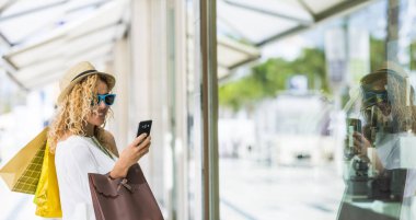 Alışveriş merkezinde alışveriş yapıp alışveriş torbaları taşıyan güzel bir kadın. Telefon kullanan kadın 