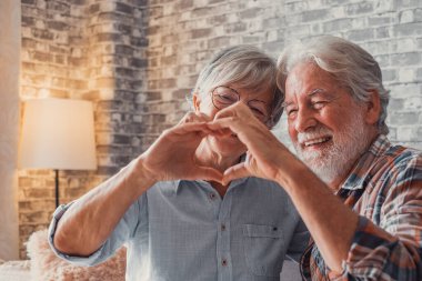 Parmaklarıyla kalp şekli oluşturan iki yetişkin büyükanne ve büyükbabanın ellerine yakın durun. Gülümseyen ve aşkta eğlenen insanlar.. 