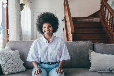 Gülümseyen bin yıllık çekici Afrikalı Amerikalı kadının portresi evdeki rahat kanepede oturuyor. Oturma odasındaki kameraya bakarak, rahat koltukta dinlenen oldukça mutlu bir zenci kadın..