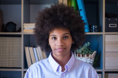 Kıvırcık saçlı, esmer, çekici bir kadının yakın plan portresi. İş yerindeki Afrikalı Amerikalı iş kadını. Kendine güvenen genç bayan kameraya bakıyor. 