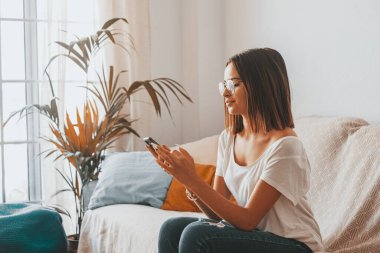 Gözlüklü ciddi bir kadın evinin oturma odasında yerde otururken cep telefonuyla mesaj atıyor. Güzel bir bayan evde akıllı telefon kullanarak vakit geçiriyor. 