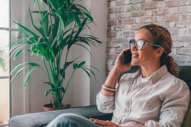 Gülümseyen kıvırcık kadın evde telefonla konuşuyor. Mutlu genç kız elinde cep telefonu tutuyor. Telefonlara cevap veriyor. 