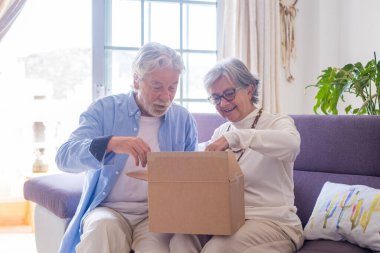 Happy mature aged older family couple unpacking carton box, satisfied with internet store purchase or unexpected gift, feeling excited of fast delivery shipping service, positive shopping experience.   clipart
