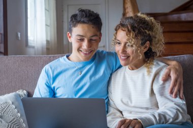 Yetişkin oğul ve orta yaşlı anne rahat bir oturma odasında oturmuş kucak defteri tutuyor komik komedi filmlerine gülüyor çevrimiçi eğlenceli internet siteleri, sanal eğlence konsepti. 