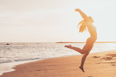Mutlu ve sağlıklı genç bir kadın kumsalda zıplıyor eğleniyor ve dışarıda yazın tadını çıkarıyor. Güzel, çekici kız oynuyor.. 