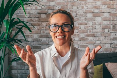 Tuğla duvarın önünde kameraya bakan gözlüklü genç bir kadının portresi. Mutlu Kafkas kadın öğretmen eğitim dersi veriyor ya da video konferansı yapıyor. 