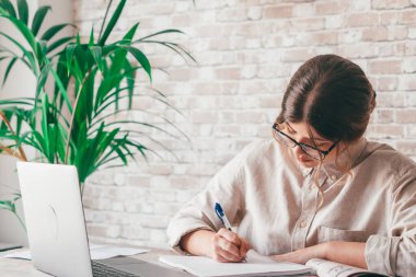 Gülümseyen kadın notlar yazıyor. Dizüstü bilgisayarda webinar çalışmalarını izliyorlar. Genç öğrenci bilgisayar dersi öğreniyor.