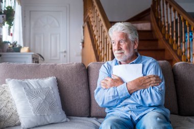 Modern apartmandaki koltukta oturmuş belgeye sarılarak bakışlarını kaçıran düşünceli bir kıdemli adam. Evdeki kanepede sağlık sigortası ya da fatura kağıdı olan yaşlı bir erkek. 